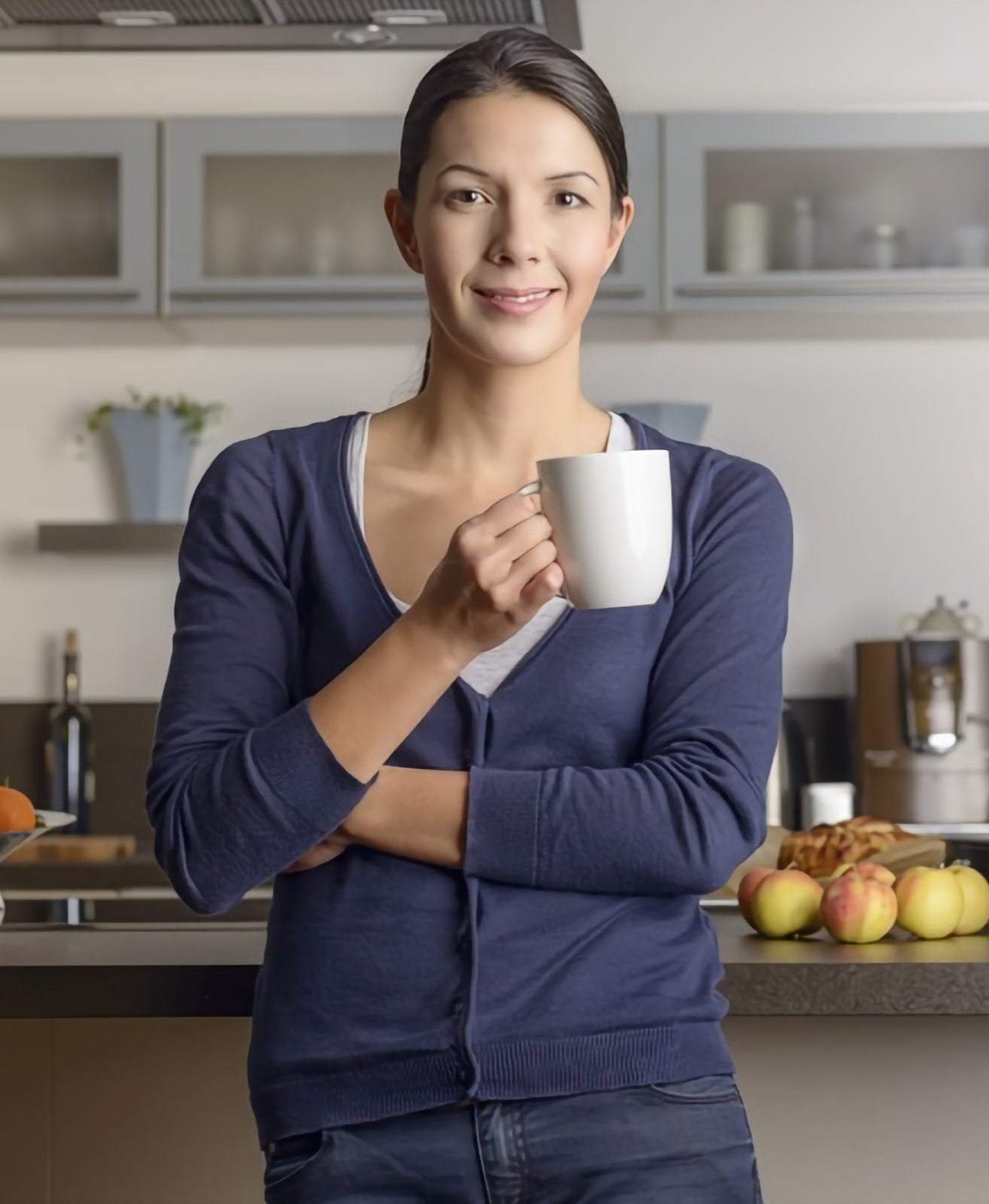 Woman holding a mug in a kitchen with apples on the counter